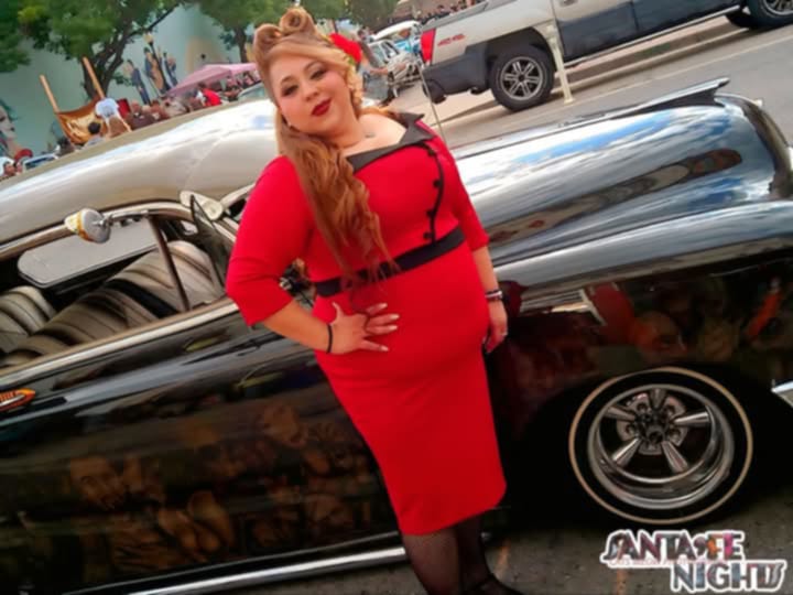 A woman in a red dress stands by a car