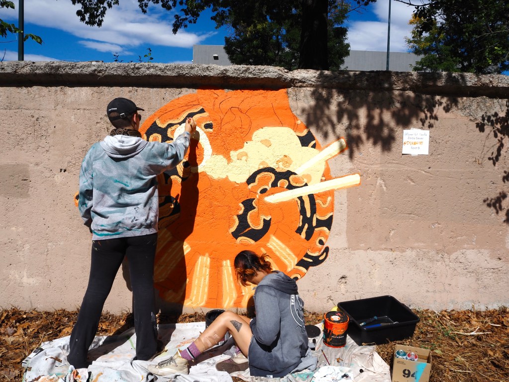 People paint an orange mural of a snake in a bowl of ramen