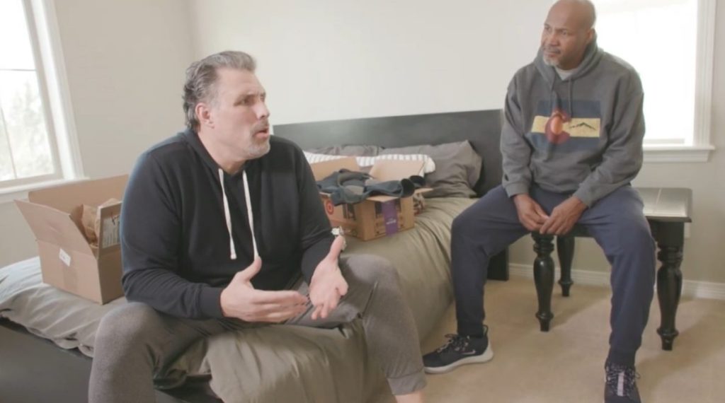 Two men sit in a bedroom and talk