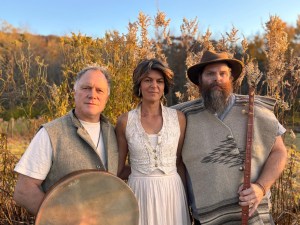 a man, woman and man hold instruments in front of a field