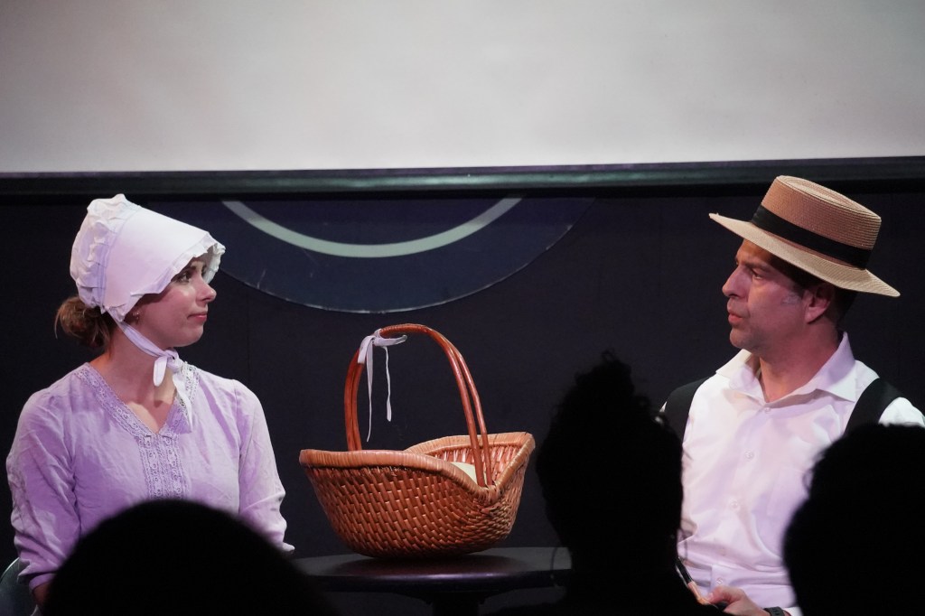 Two people sit across from each other in old timey garb.
