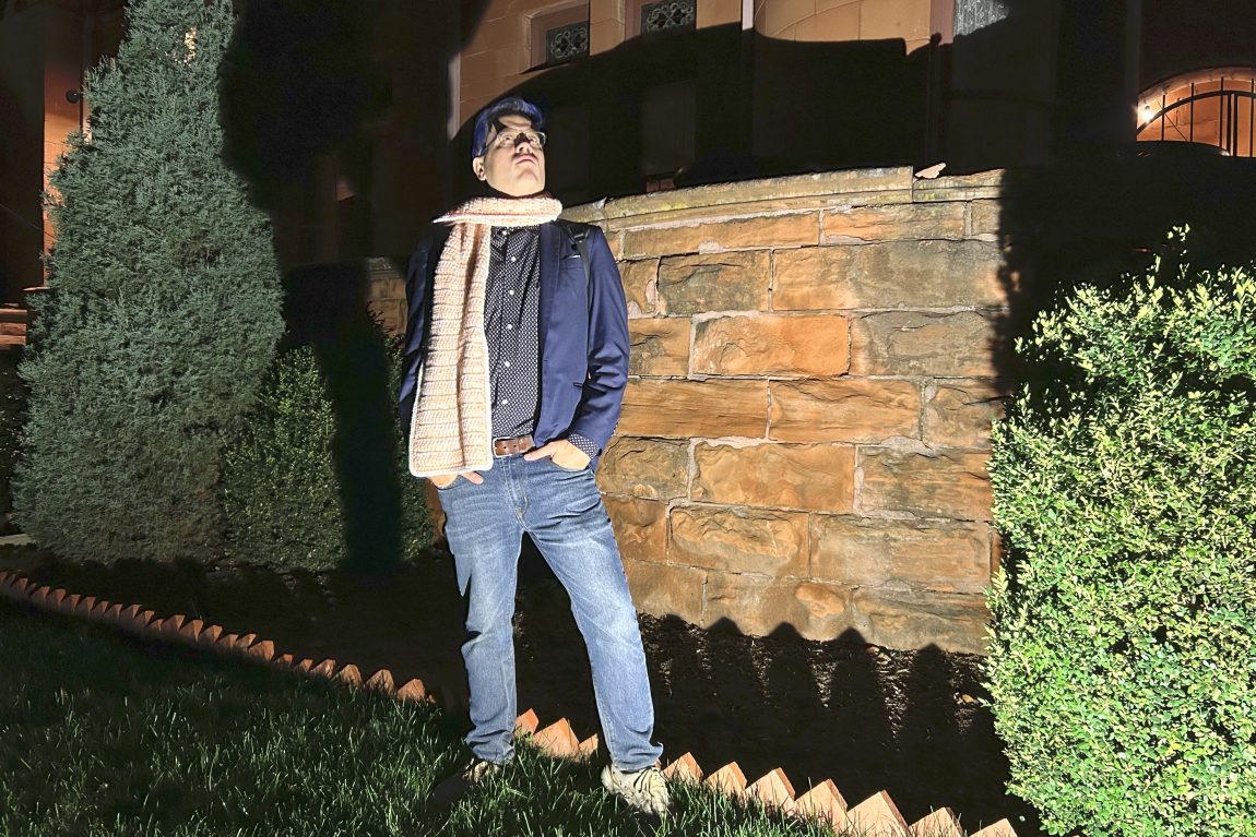 man in a crochet scarf, standing outside the Patterson Inn at night