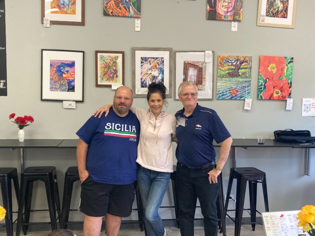 three people posing in front of art in a wall