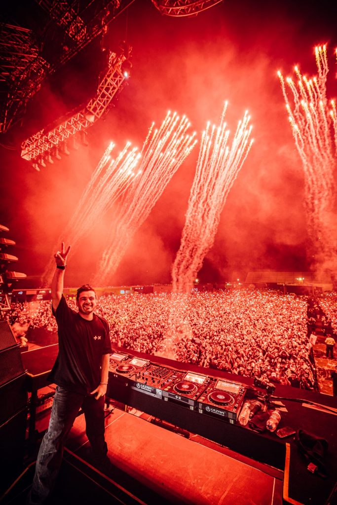 Martin Garrix at the DJ booth with fireworks behind him