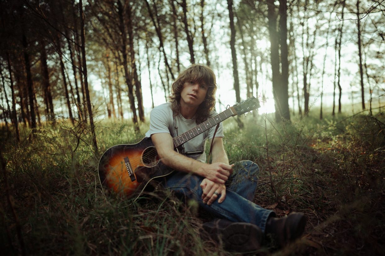 Jesse Welles in the woods with a guitar