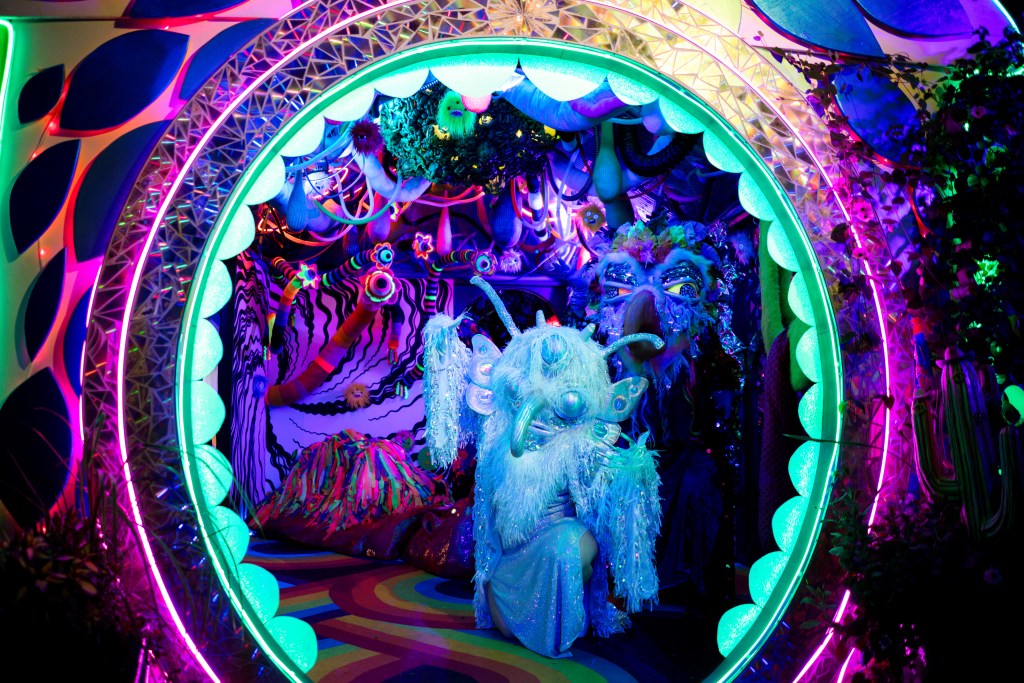 Two masked performers in a colorful immersive environment.