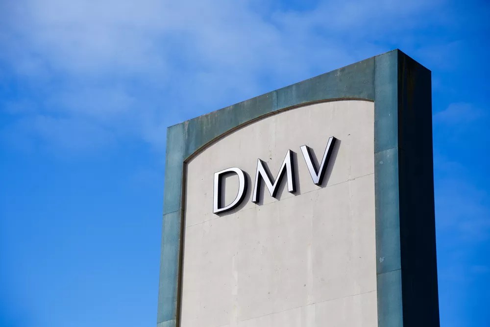 A DMV sign outside against a blue sky.