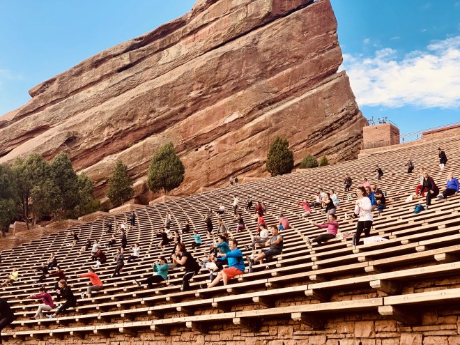 a crowd does yoga poses on red rocks amphitheatre steps