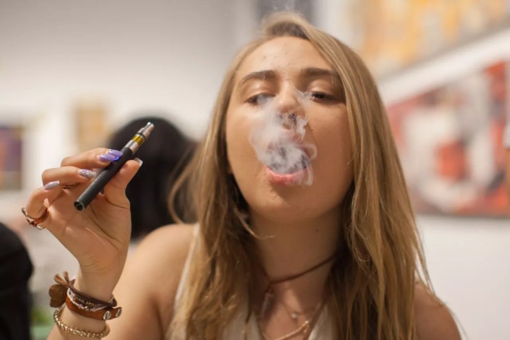 Young blonde woman hits vape.