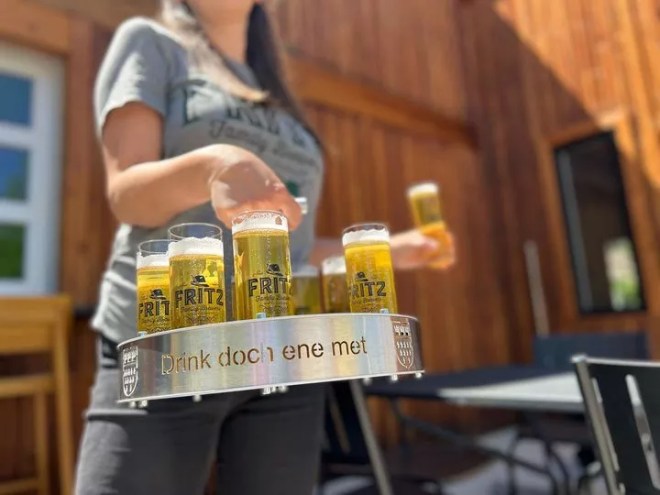 a person carrying a metal tray of filled beer glasses