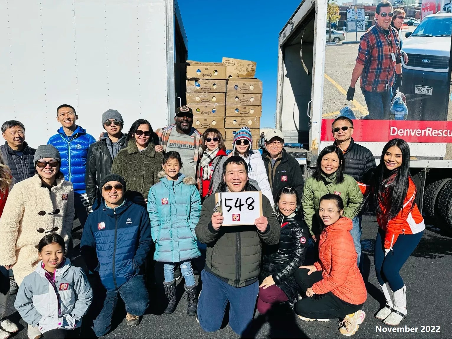 A crowd of people stand in front of two large trucks, with a sign that has "538" written on it.
