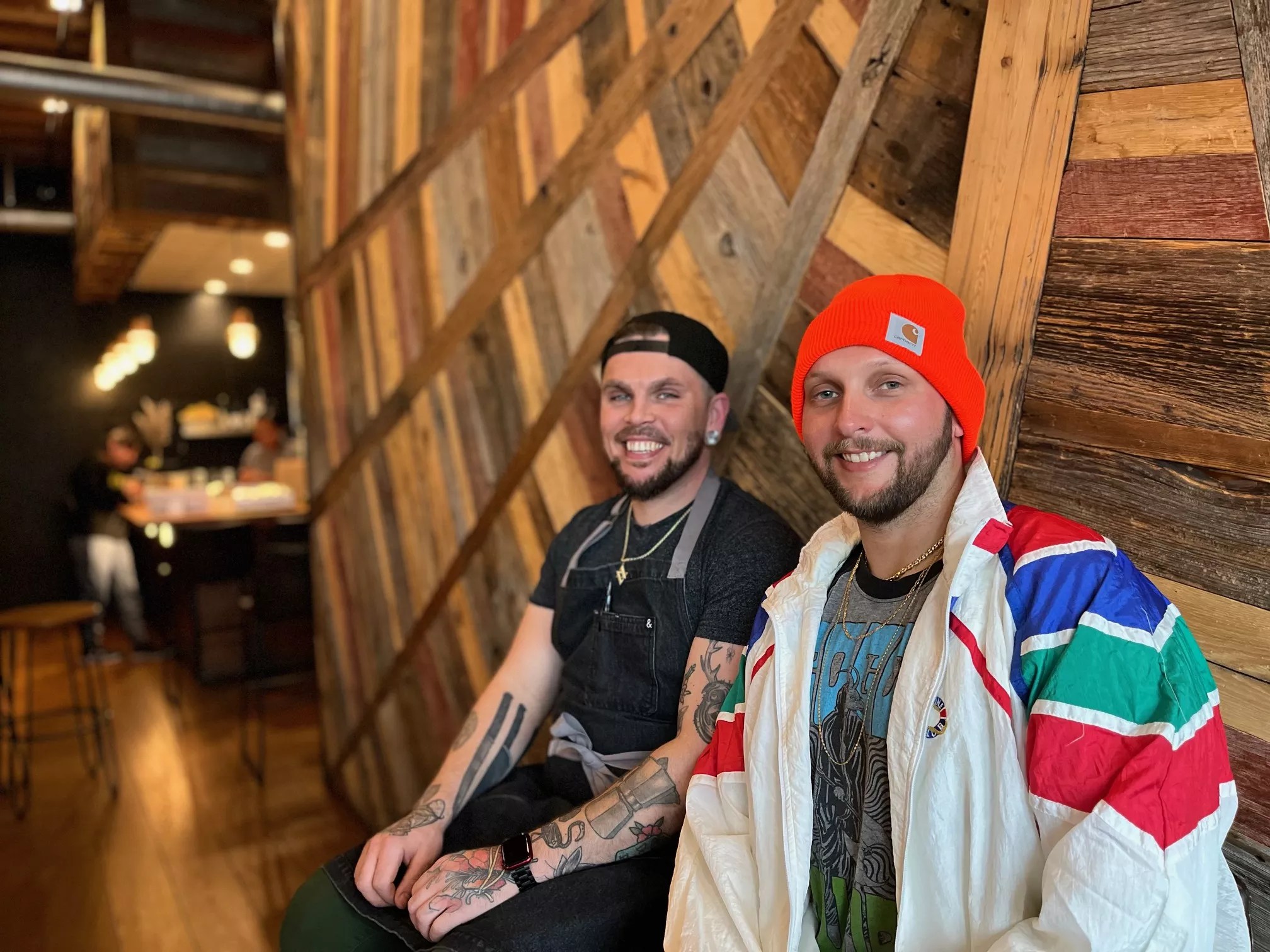 Two men in beanies sit and smile