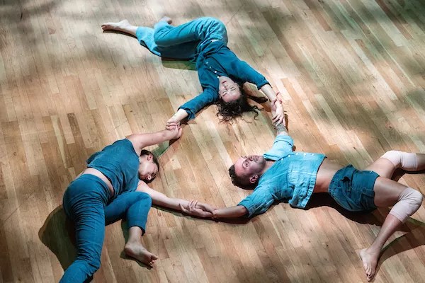 three people wearing blue lie on the floor holding hands