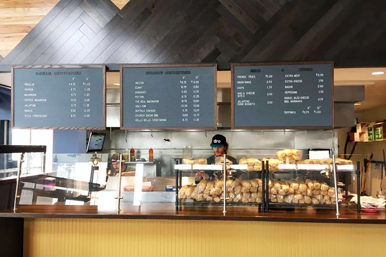 a man in a hat standing behind a sandwich shop counter