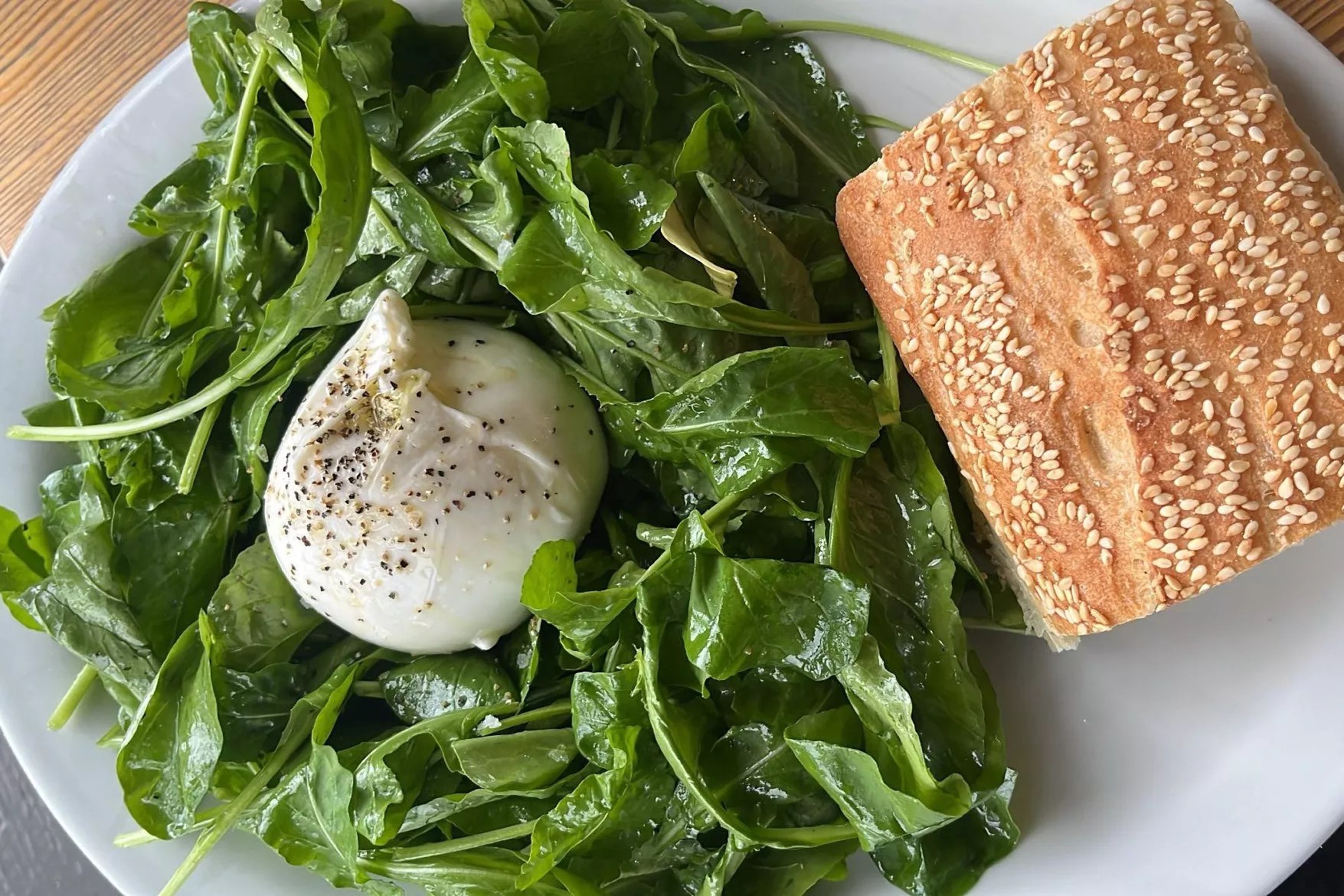 A ball of cheese on greens with a side of bread.