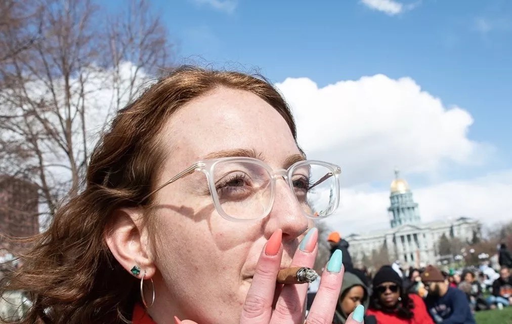 A woman smokes a joint at Civic Center Park at the 2023 4/20 festival, in front of the State Capitol Building.