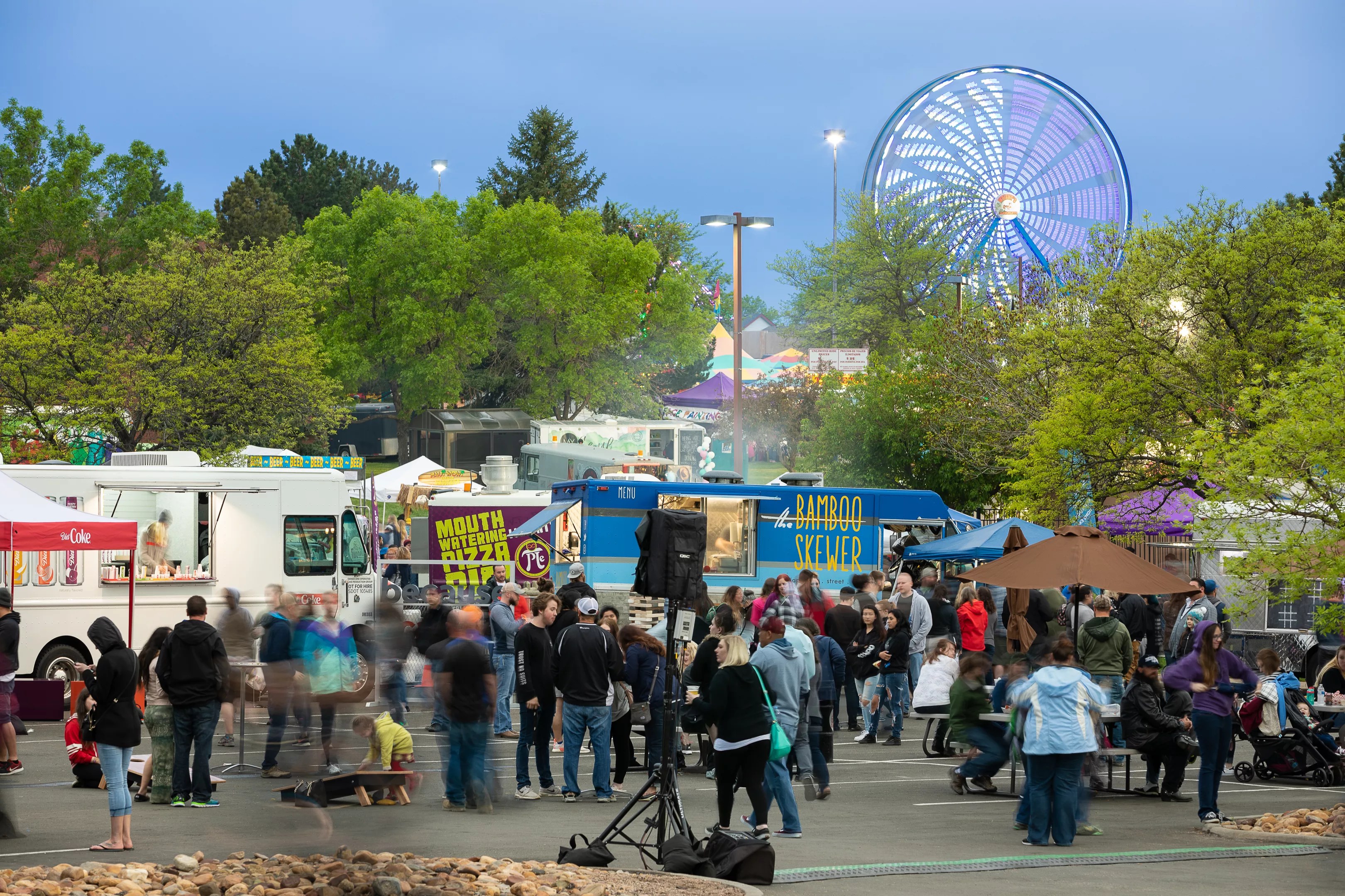 a crowd of people gathered around food trucks with a ferris wheel in the background.