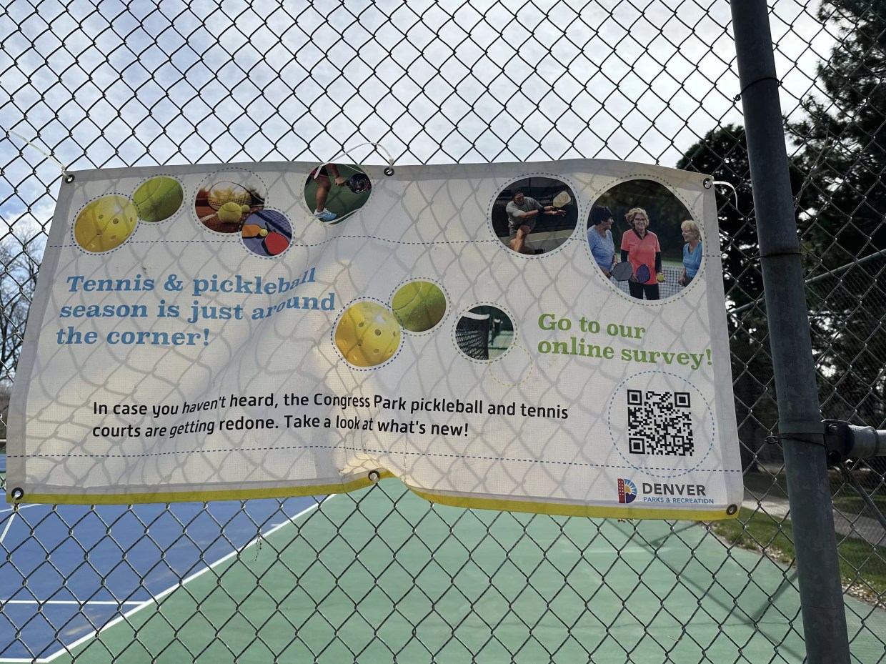 A banner proclaiming it is almost pickleball and tennis season on a fence at a public park.