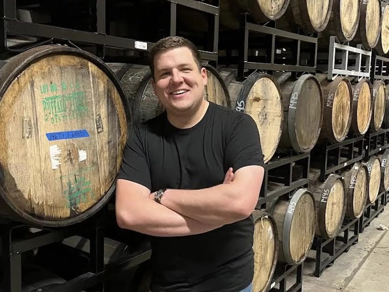 a man in a black t shirt stands in front of wooden barrels