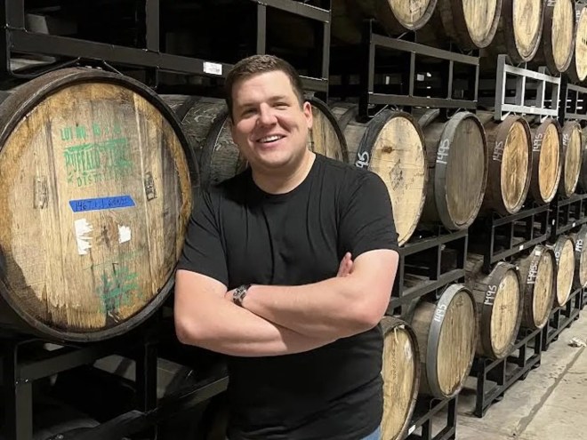 a man in a black t shirt stands in front of wooden barrels