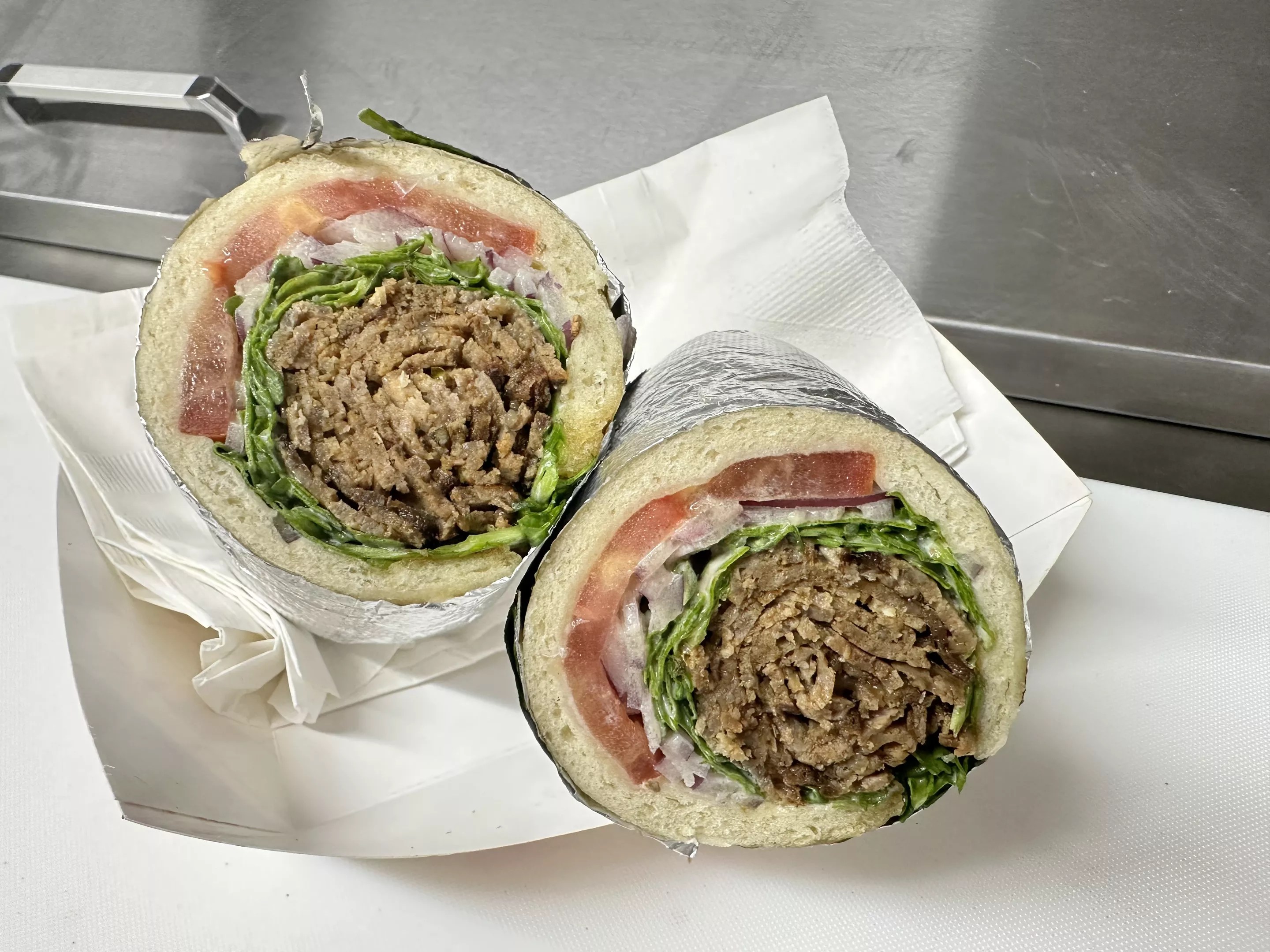 a beef and lamb gyro wrapped in pita with tomatoes and arugula