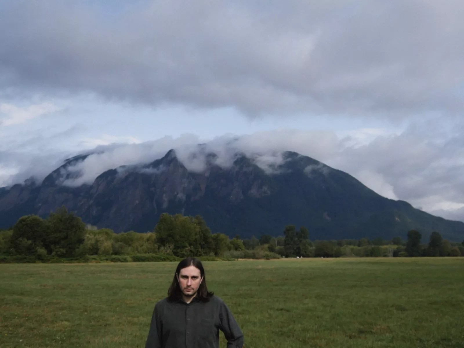 man stands in field in front of mountain