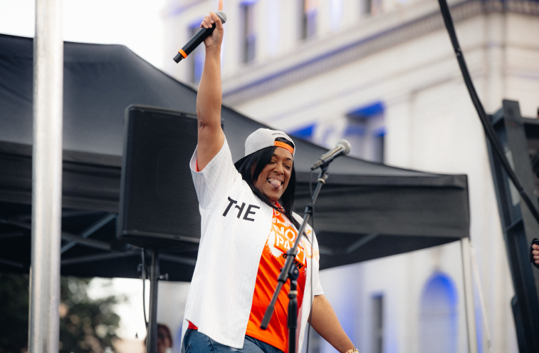 woman holds up a microphone on stage and smiles