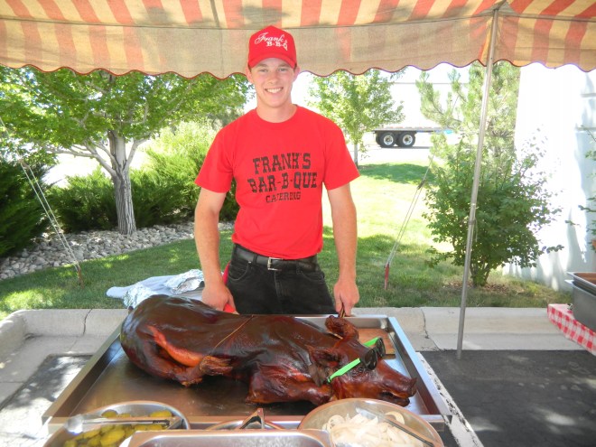 a man in a red shirt standing in front of a whole barbecued pig