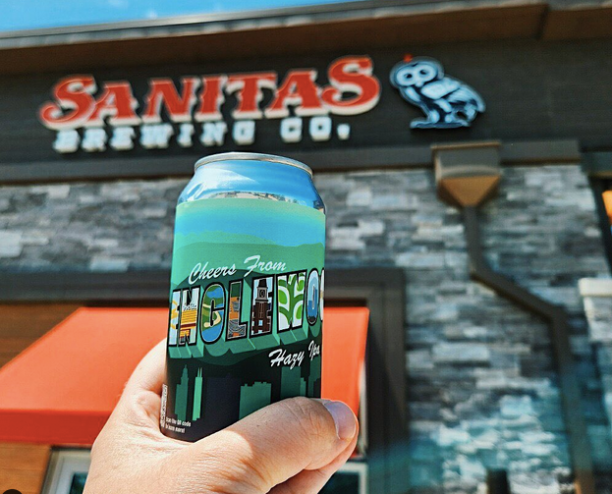 hand holding a can of beer in front of a building