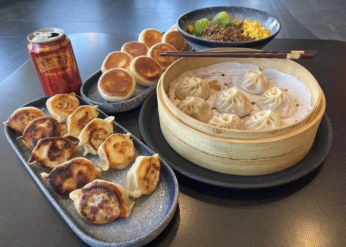 two plates covered in dumlpings, dumlpings in a steam basket and a bowl of noodles
