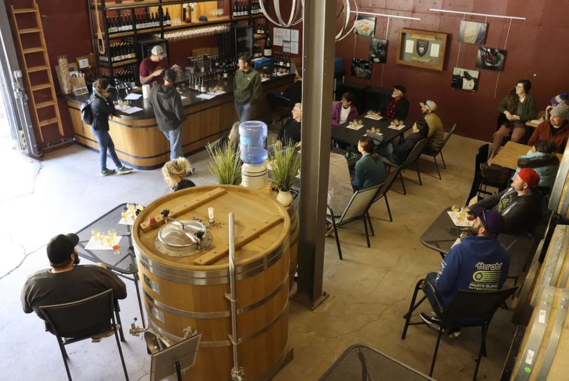 people sitting at tables in a room with a big wooden barrel