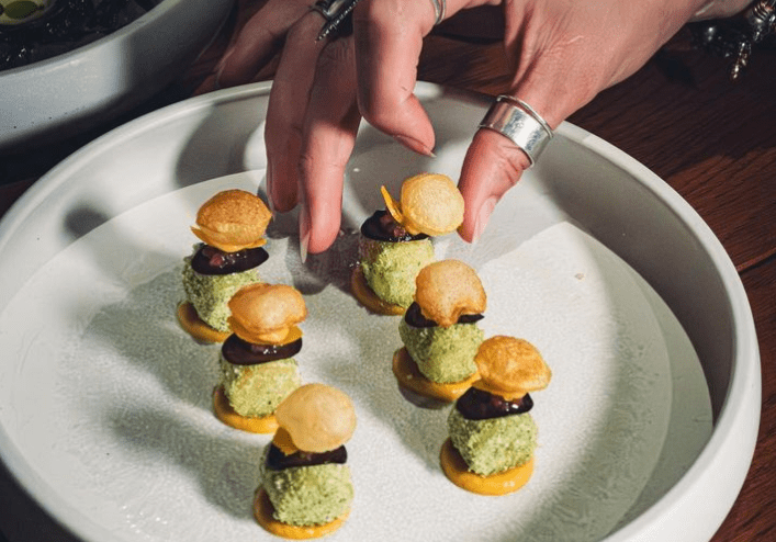 a hand reaching for a small appetizer on a place