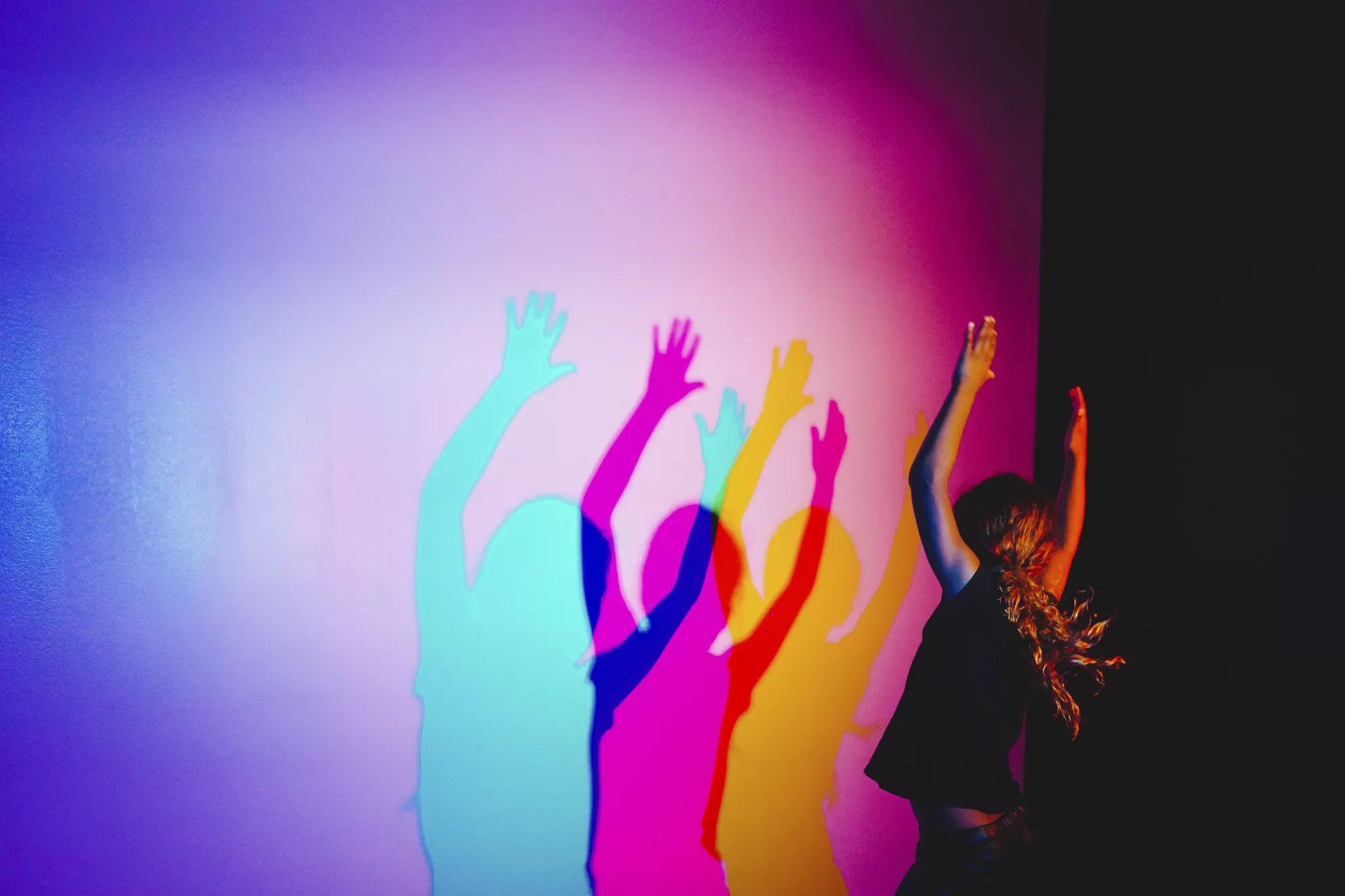 a person makes colorful shadows in pink and blue on a purple wall.