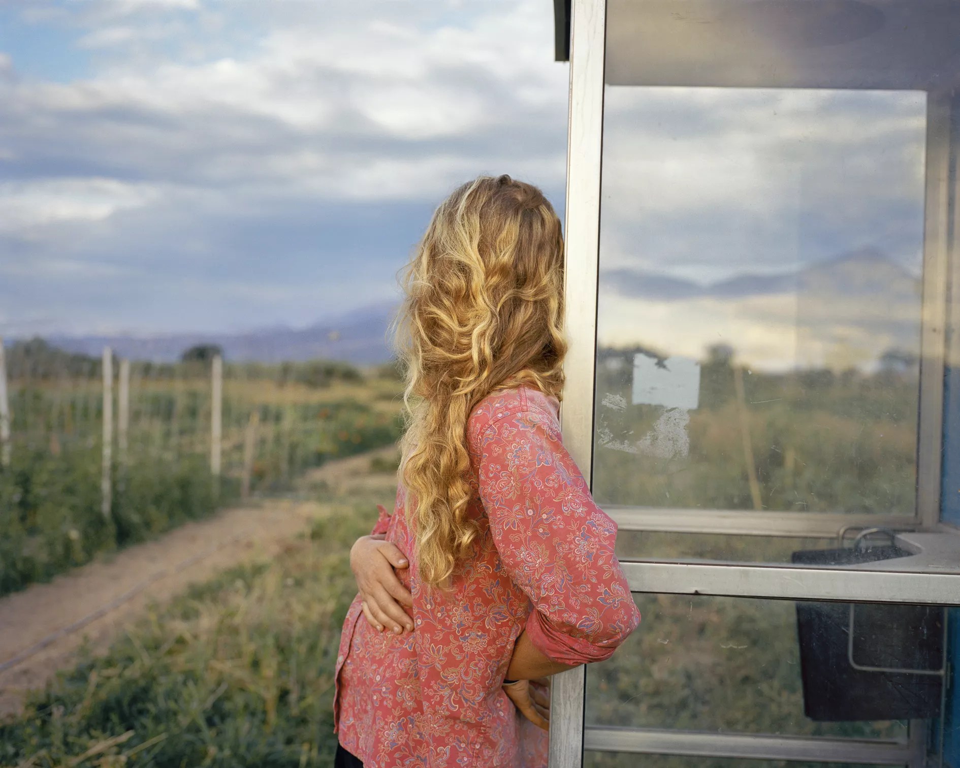 blonde woman leaning on a window looking out at the countryside