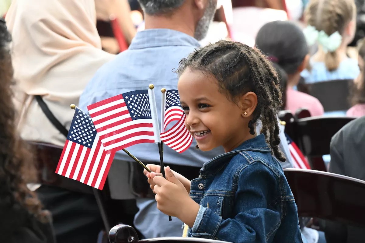 Nael Welday from Angola waves three American flags at a citizenship ceremony that took place at the Children's Museum of Denver on Thursday, July 20.