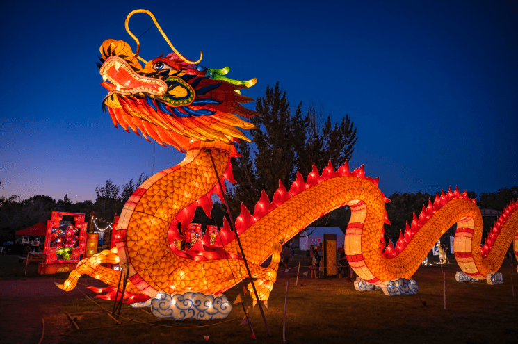 Large glowing dragon lantern made of orange paper against a dark blue sky.