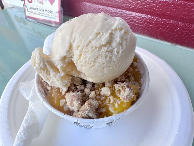 a scoop of vanilla ice cream on top of peach cobbler in a cup