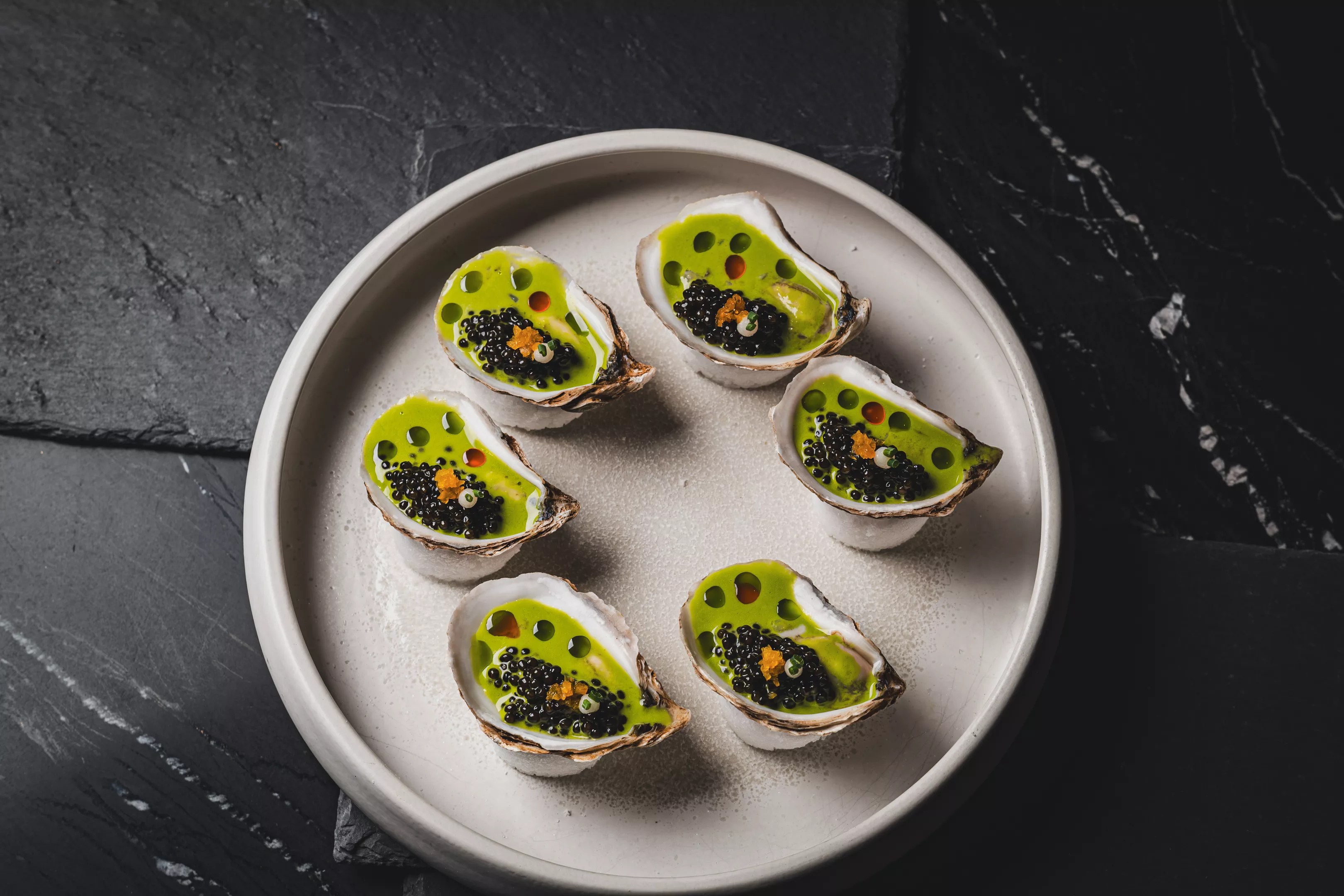 a plate of oysters with green liquid in the shells