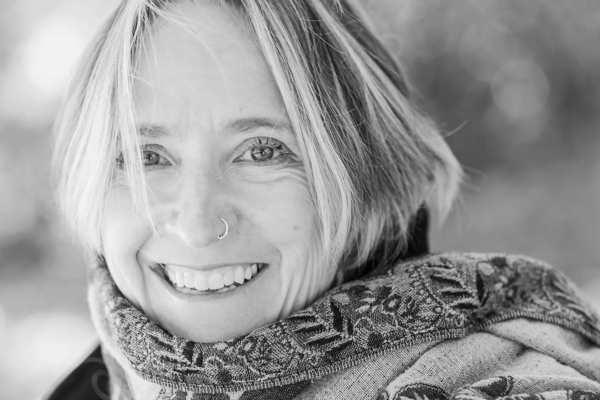 a black and white photo of a smiling blonde woman wearing a scarf