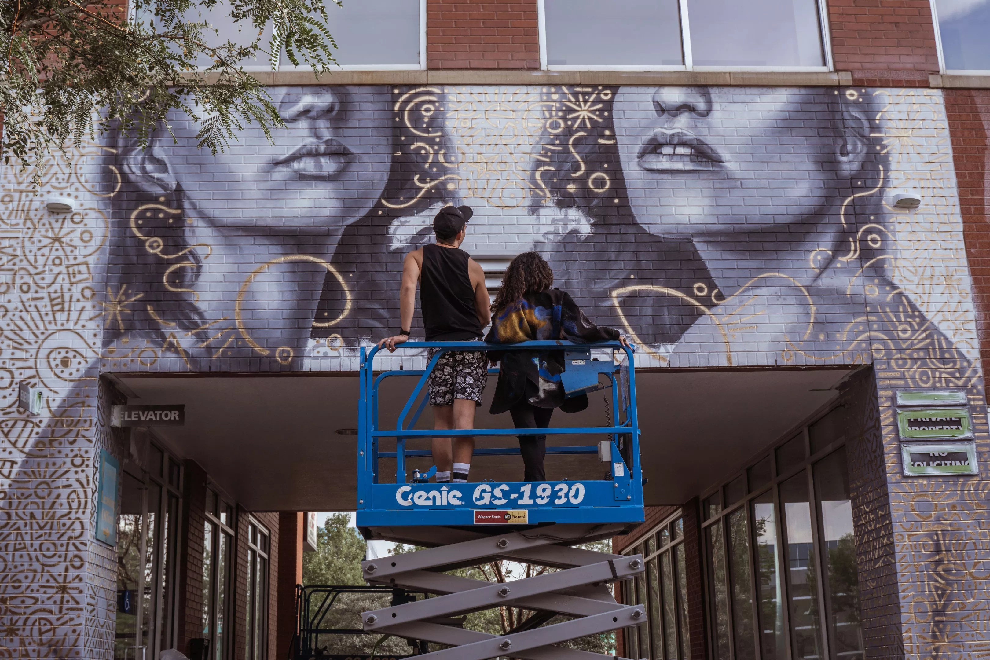 Two muralist admire their work from a crane