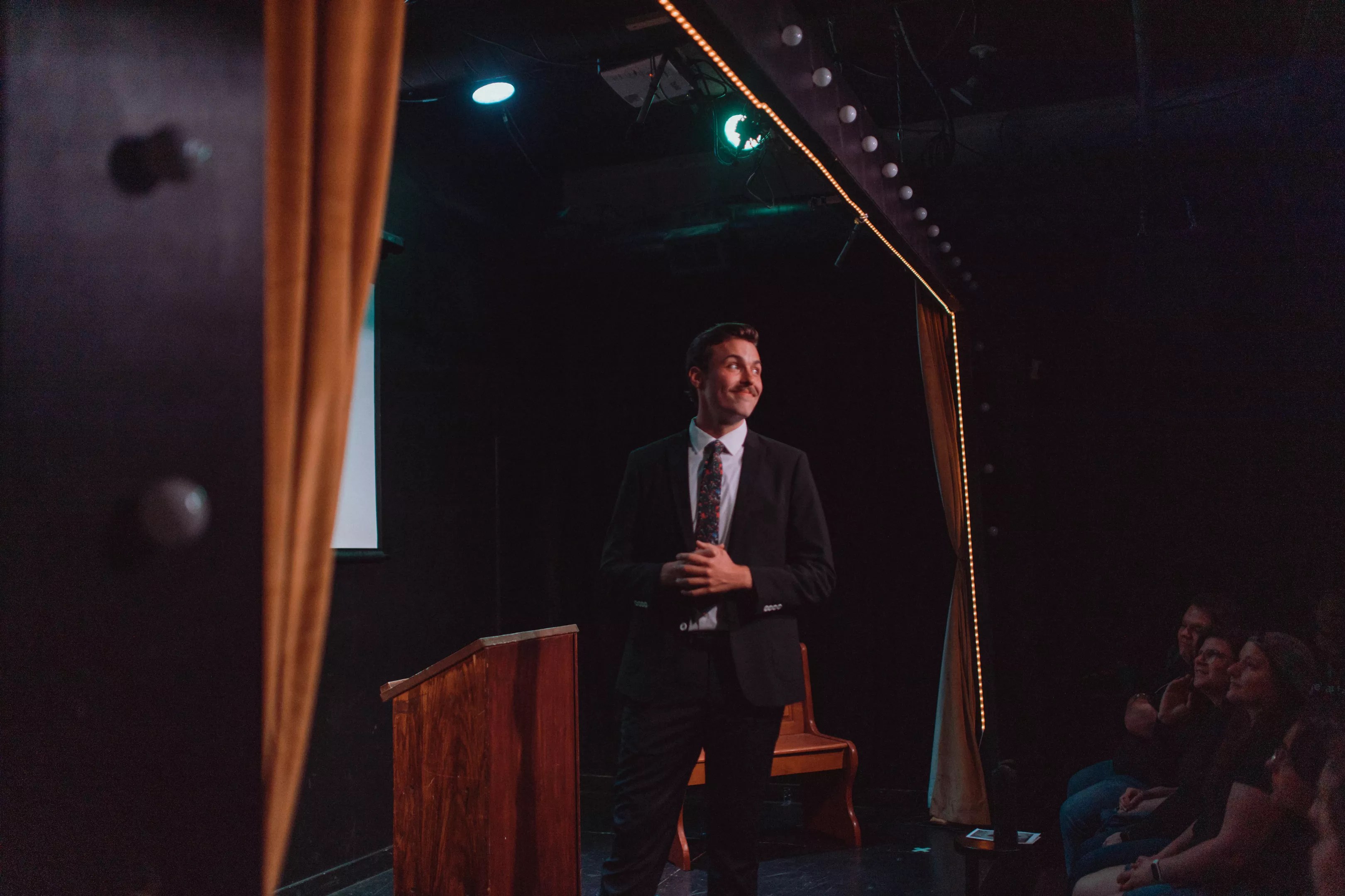 moustached young man in a suit and tie on a stage