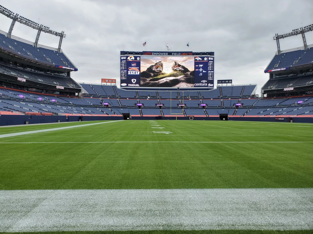 A giant scoreboard at the end of a stadium with a grassy field.