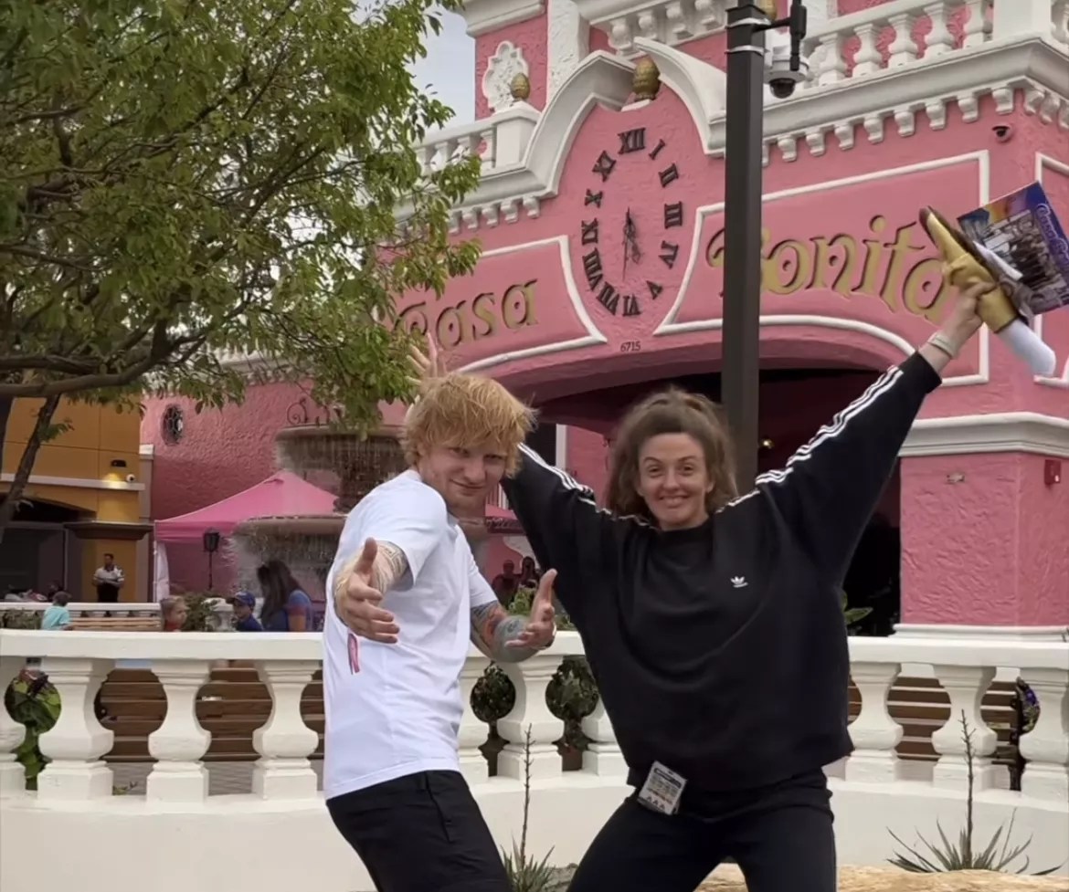 a man and woman strike poses outside of a pink building