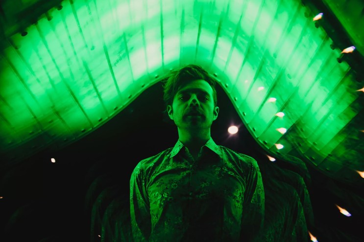 a man stares seriously at the camera while cast in green lighting.