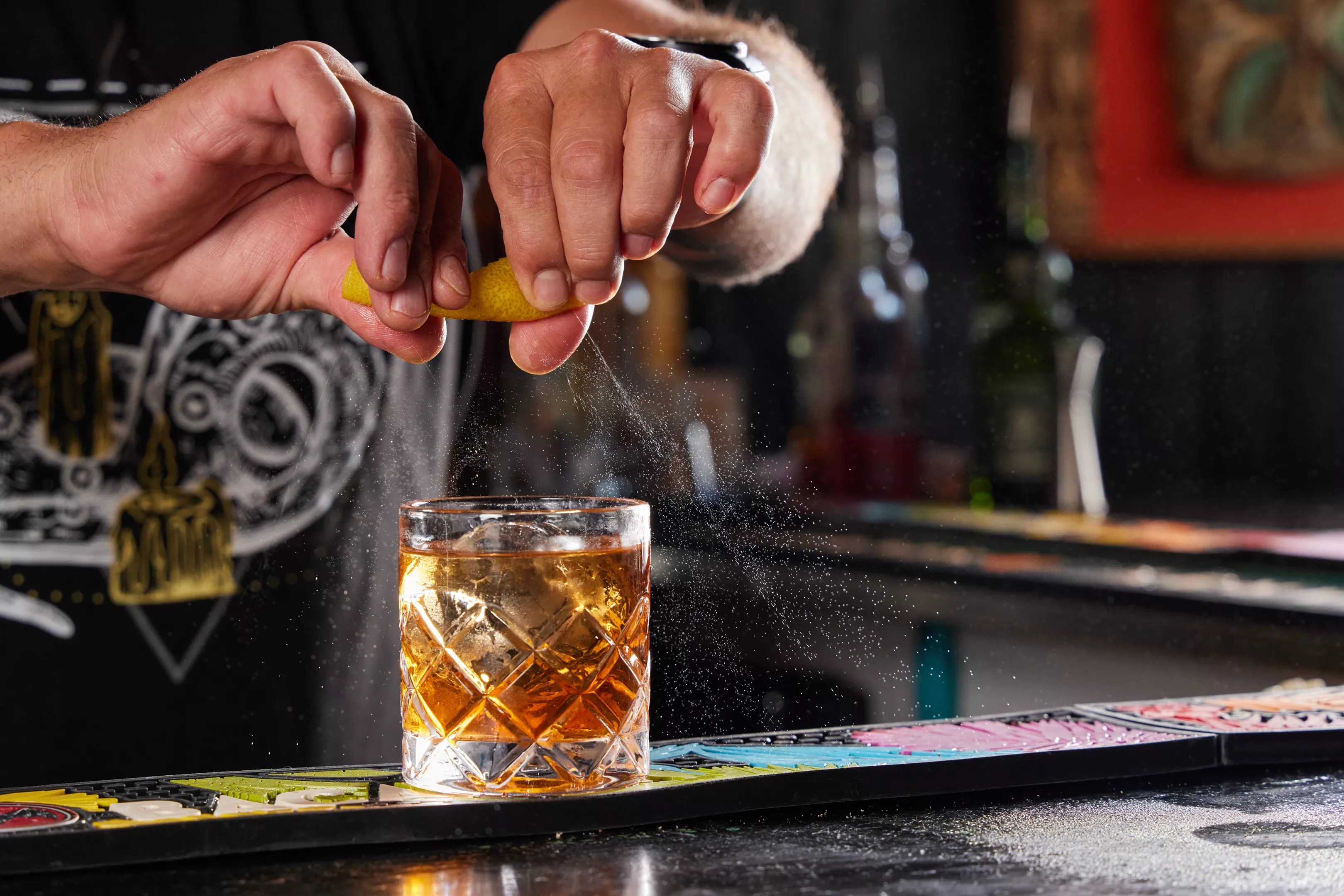 hands squeeze citrus in glass of brown liquid