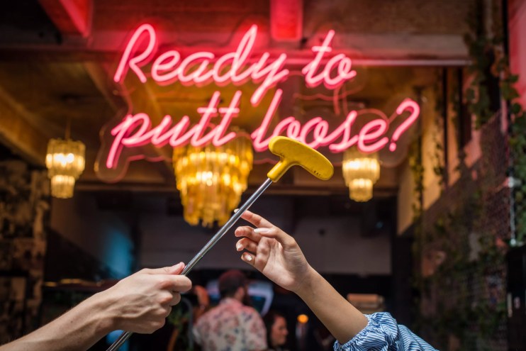 hand reaching for a putter in front of a neon sign