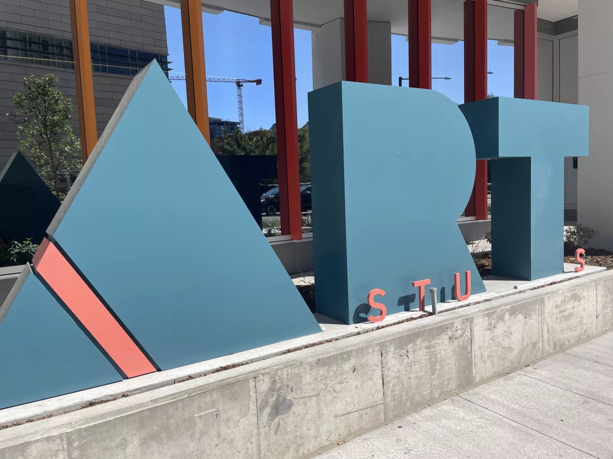 A huge, teal A-R-T sign in front of an orange-columned building.