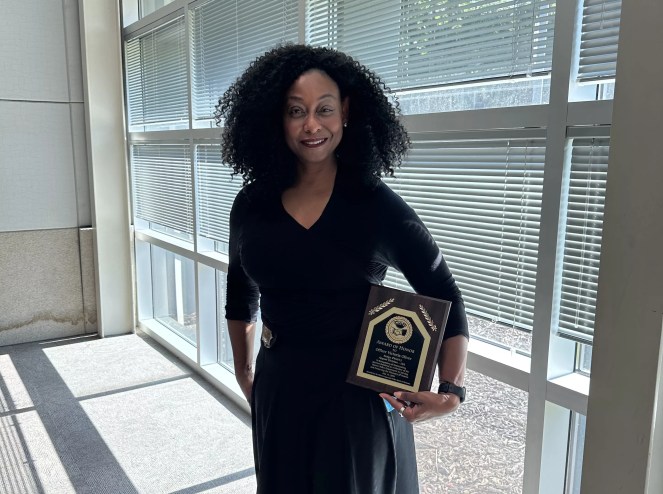Officer Victoria Oliver standing with her Citizens Appreciate Police (CAP) award that she received for buying a plane ticket for a woman to escape domestic violence.