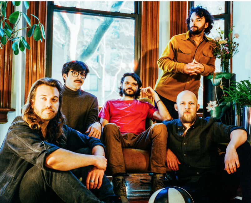 five men sitting in a wood pannel room