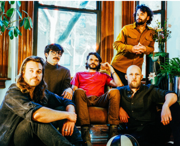 five men sitting in a wood pannel room